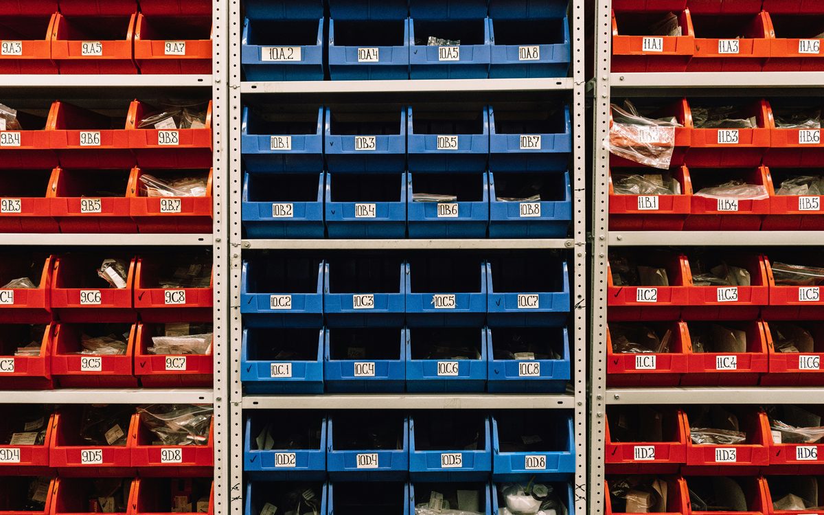 Rows of red and blue parts bins on warehouse shelving, each labelled with a bin location